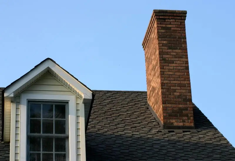 House roof with a brick chimney against a clear sky in Dallas, TX 