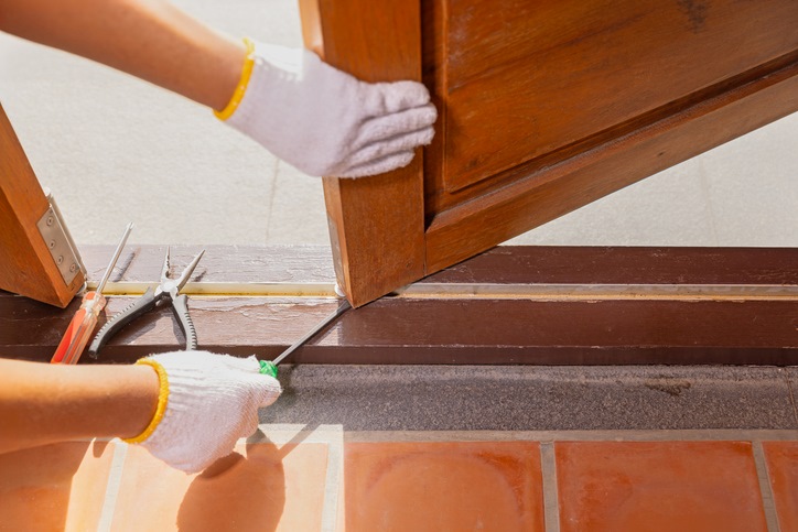 A person fixing a stuck wooden door with tools in Dallas, TX
