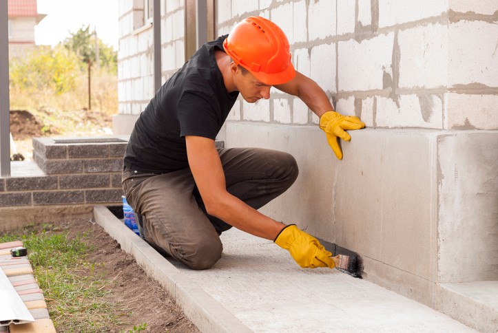Worker applying waterproof sealant on foundation wall in Dallas, TX