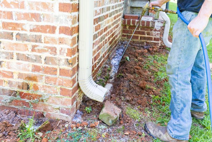 A Worker cleaning around a foundation with a hose for drainage in Dallas, TX